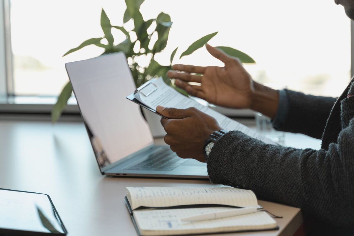 Buyer reviewing a document on a clipboard beside an open laptop at a desk