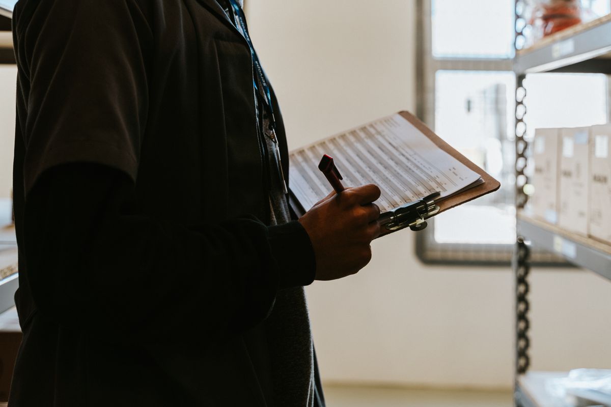 Warehouse worker recording inventory information on a clipboard beside storage shelving