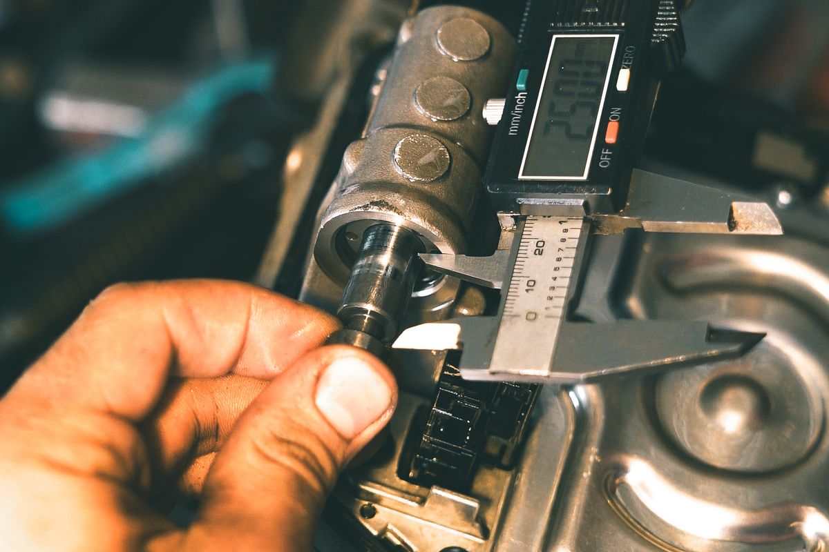 Technician measuring a metal component with a digital caliper in a workshop