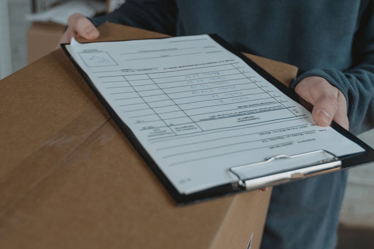 Worker holding an order checklist on a clipboard beside a labelled cardboard shipping box